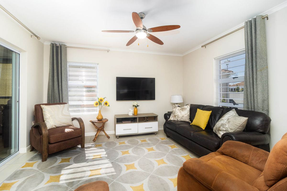 A well-lit living room featuring tiled flooring, a ceiling fan, and sliding glass doors providing access to the outdoor area.