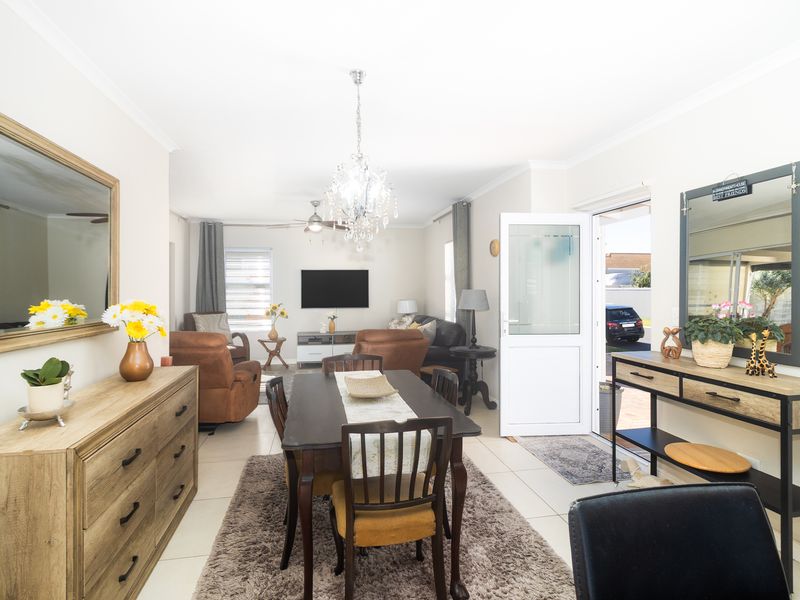 Open-plan living and dining area featuring tiled flooring, a central crystal chandelier, and direct access to the exterior via a uPVC door.