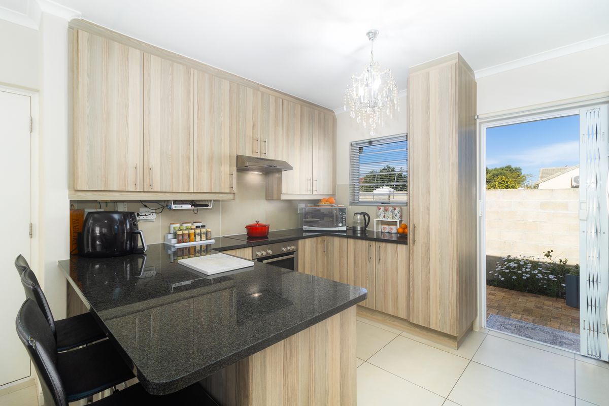 Modern kitchen featuring light wood-grain cabinetry, dark granite countertops, built-in oven, extractor fan, and direct access to an outdoor patio area.