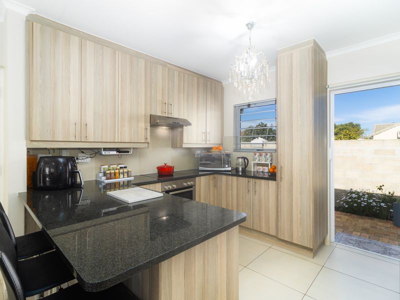 Modern kitchen featuring light wood-grain cabinetry, dark granite countertops, built-in oven, extractor fan, and direct access to an outdoor patio area.