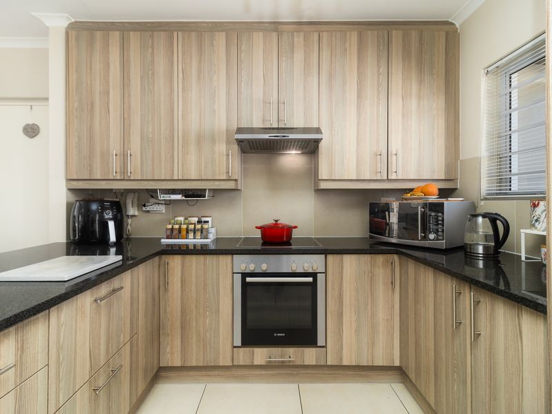 A well-maintained kitchen featuring wood-grain cabinetry, granite countertops, a built-in oven, electric hob, and an extractor fan.