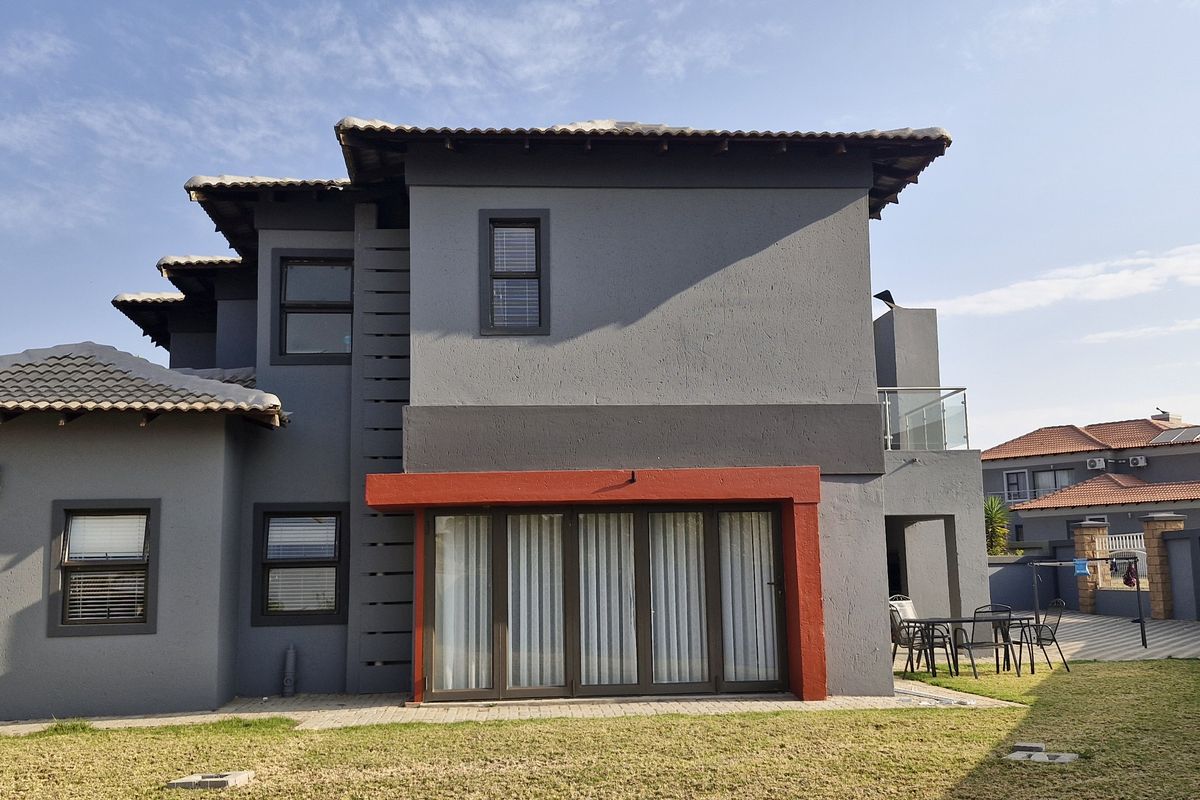 Rear view of a modern two-story house featuring dark grey exterior walls, a tiled roof, and a paved patio area with sliding glass doors.