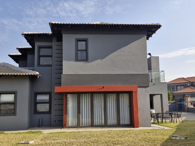 Rear view of a modern two-story house featuring dark grey exterior walls, a tiled roof, and a paved patio area with sliding glass doors.