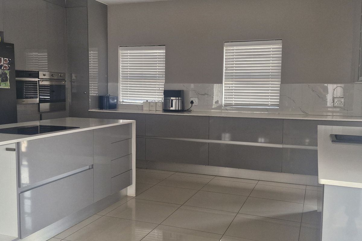Modern kitchen featuring high-gloss grey cabinetry, quartz countertops, a central island with integrated cooktop, and marble-look splashback with tiled flooring.