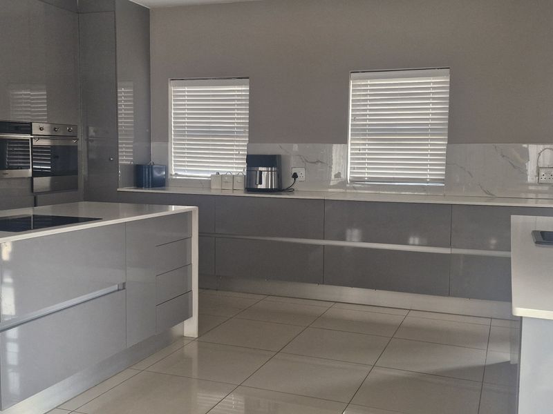 Modern kitchen featuring high-gloss grey cabinetry, quartz countertops, a central island with integrated cooktop, and marble-look splashback with tiled flooring.