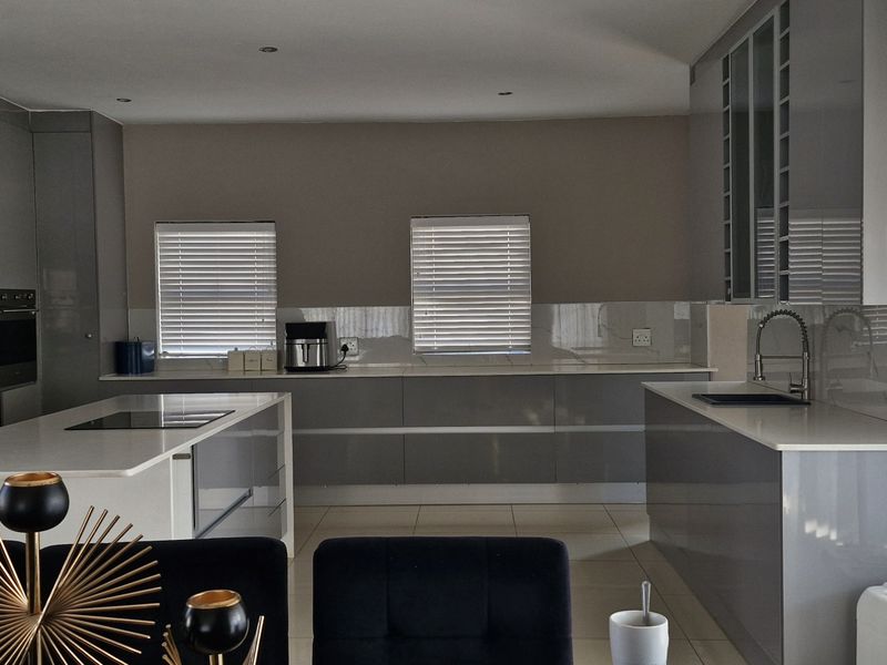Modern kitchen featuring sleek grey cabinetry, a central island with integrated cooktop, stone countertops, and high-quality finishes throughout.