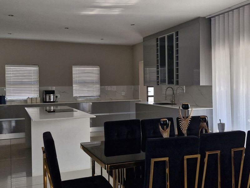 Modern open-plan kitchen and dining area featuring sleek grey cabinetry, stone countertops, a central island, and large windows with elegant sheer curtains.