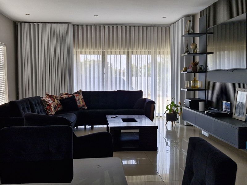Modern living room featuring a sleek slatted feature wall, built-in media console, polished porcelain floor tiles, and large sliding doors with vertical blinds.
