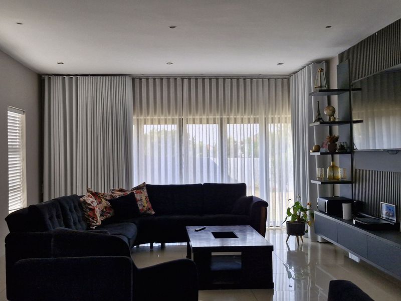 A modern living room featuring a stylish slatted feature wall, built-in media cabinetry, recessed lighting, and large windows with floor-to-ceiling curtains.