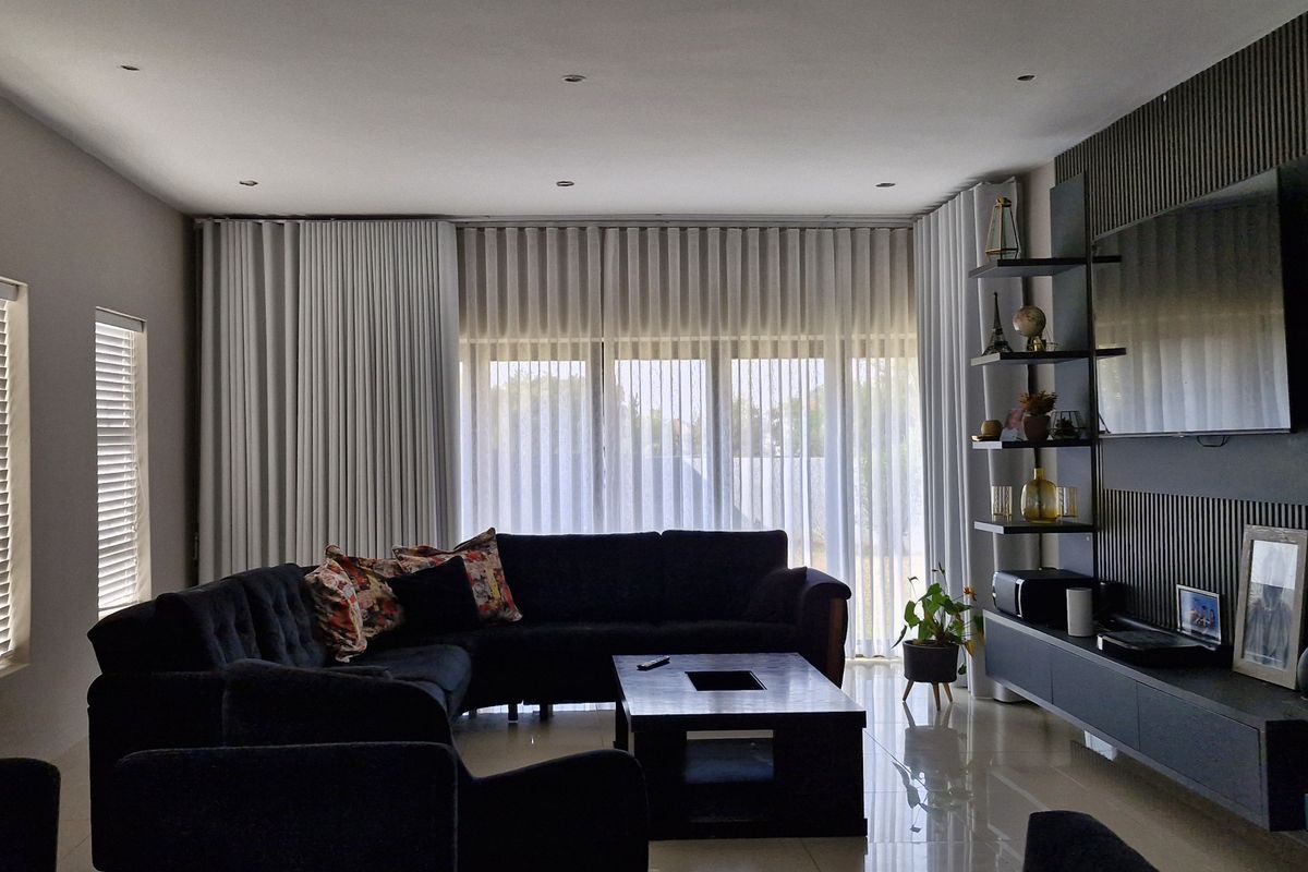 A modern living room featuring a stylish slatted feature wall, built-in media cabinetry, recessed lighting, and large windows with floor-to-ceiling curtains.