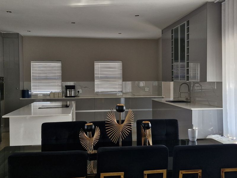 Modern open-plan kitchen featuring high-gloss cabinetry, stone countertops, a central island, and integrated fixtures, seamlessly flowing into the dining area.
