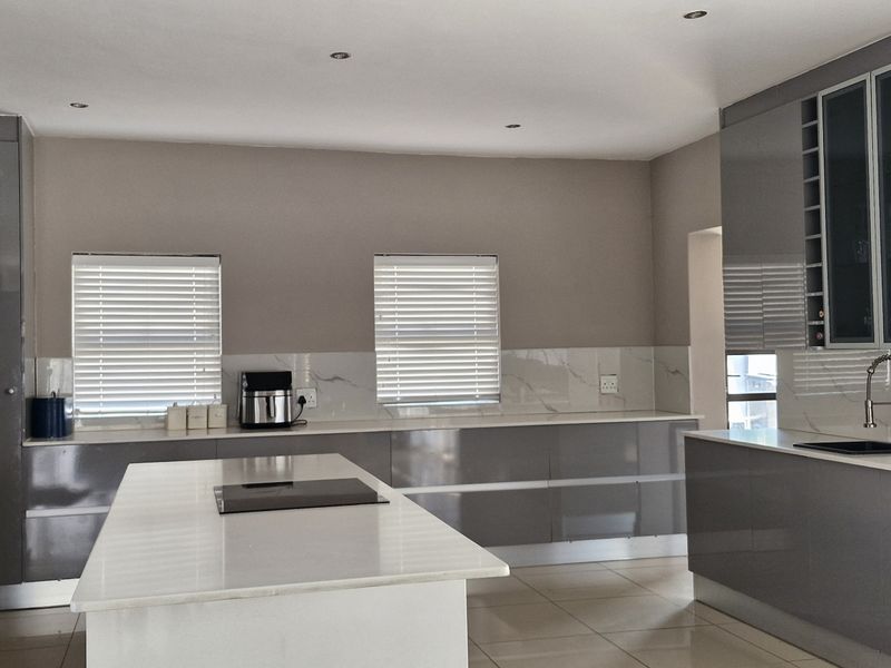 Modern kitchen featuring high-gloss grey cabinetry, a central island with stone countertops, marble-look backsplash, and integrated fixtures.