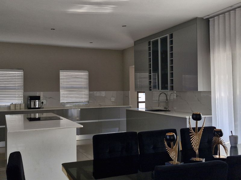 Modern open-plan kitchen featuring sleek grey cabinetry, a central island with quartz countertops, and high-end finishes, seamlessly integrated with the dining area.