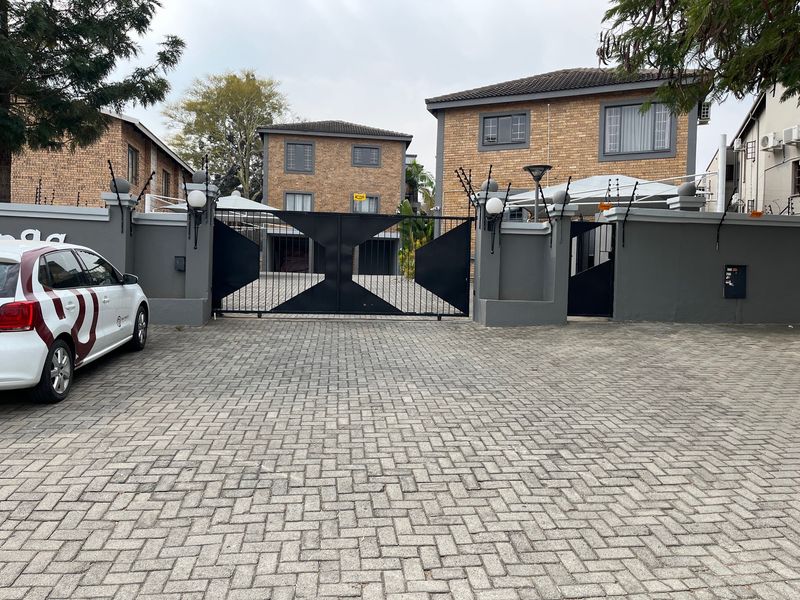 Front view of a secure apartment complex featuring a brick facade, paved driveway, and gated entrance with electric fencing.