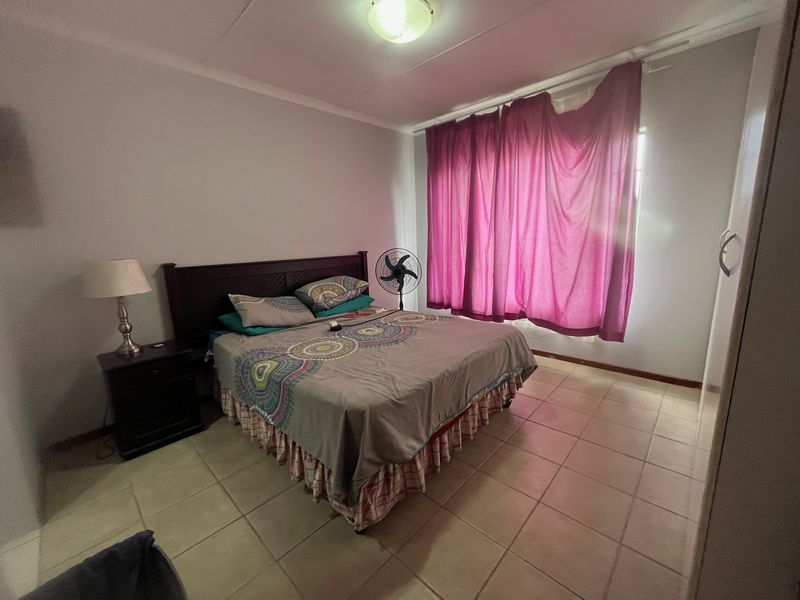 A functional bedroom featuring tiled flooring, a built-in cupboard, and natural light through a window with curtains.