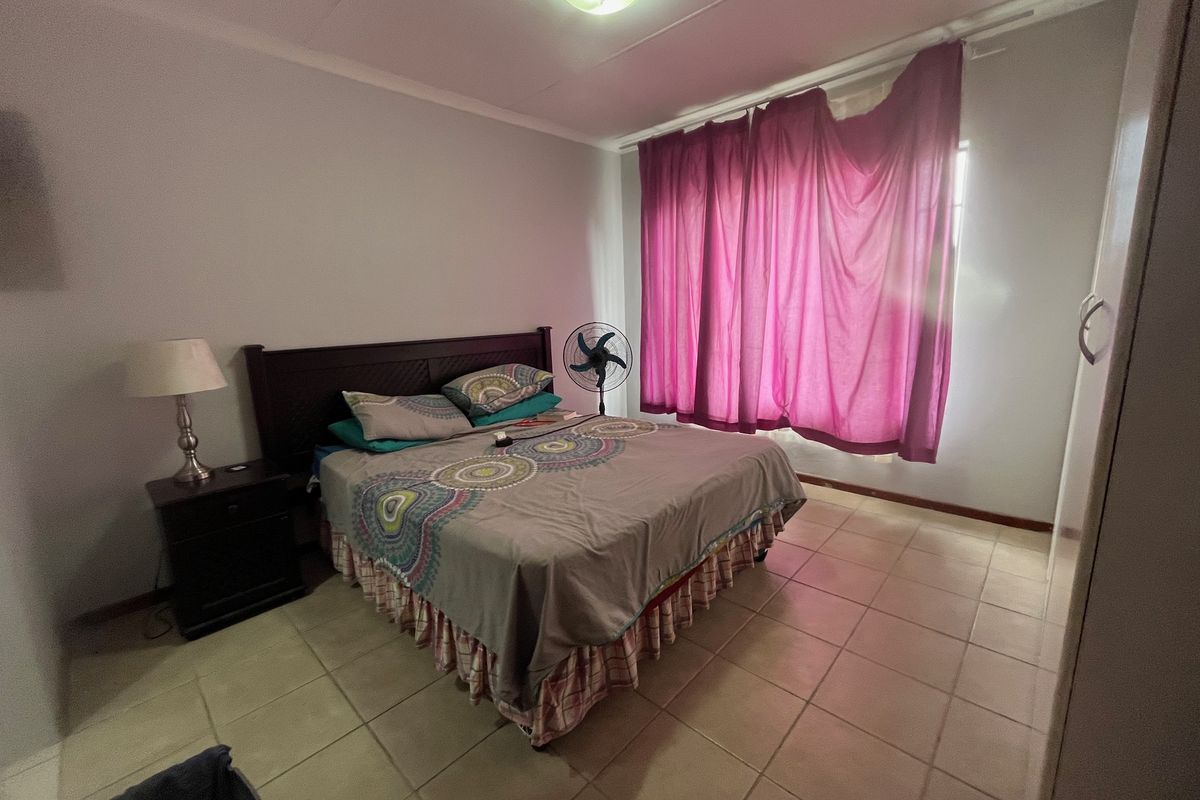 A functional bedroom featuring tiled flooring, a built-in cupboard, and natural light through a window with curtains.