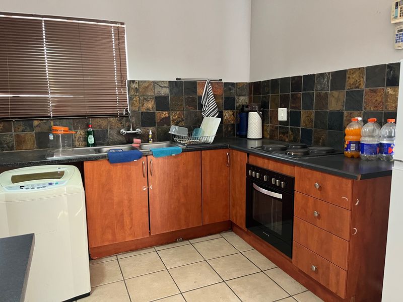 Functional kitchen featuring wood-tone cabinetry, stone tile backsplash, built-in oven, electric hob, and tiled flooring with integrated sink and laundry appliance space.