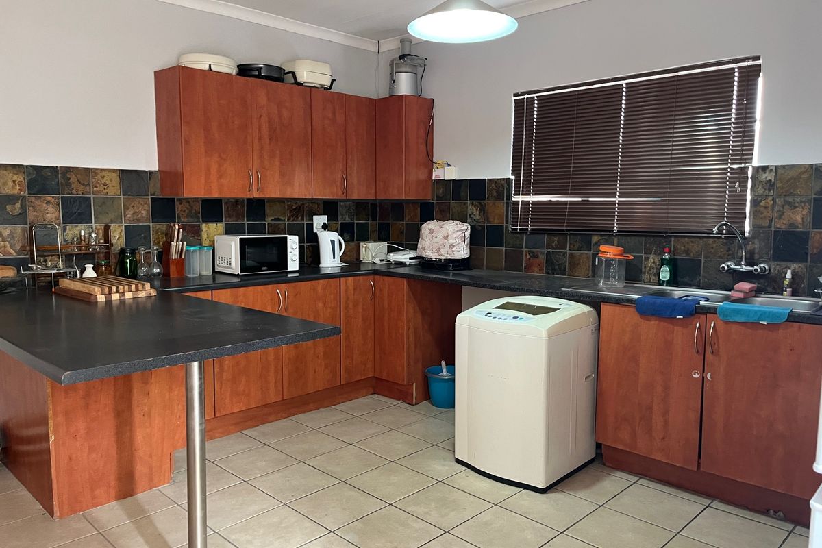 Functional kitchen featuring wood-look cabinetry, stone tile backsplash, laminate countertops, and tiled flooring with integrated sink and breakfast bar area.