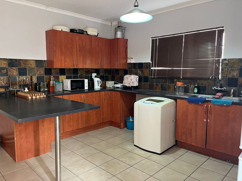 Functional kitchen featuring wood-look cabinetry, stone tile backsplash, laminate countertops, and tiled flooring with integrated sink and breakfast bar area.