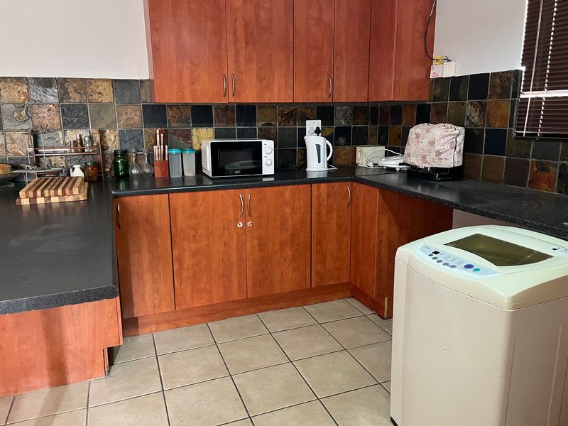 A functional kitchen featuring wood-tone cabinetry, dark laminate countertops, and a decorative stone-look tile backsplash with ceramic floor tiling.