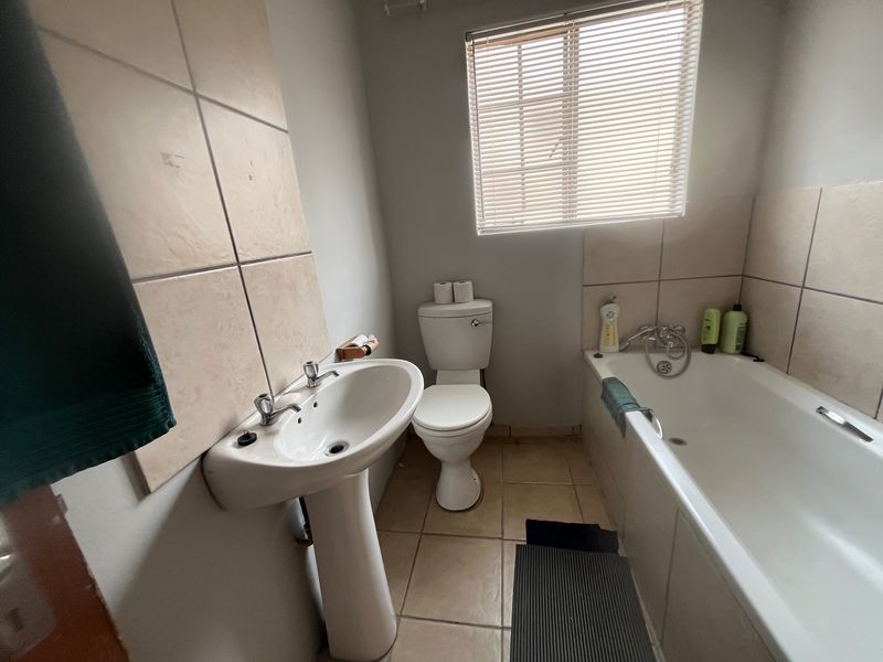 A functional bathroom featuring a pedestal basin, standard toilet, and a bathtub with tiled splashbacks and flooring.