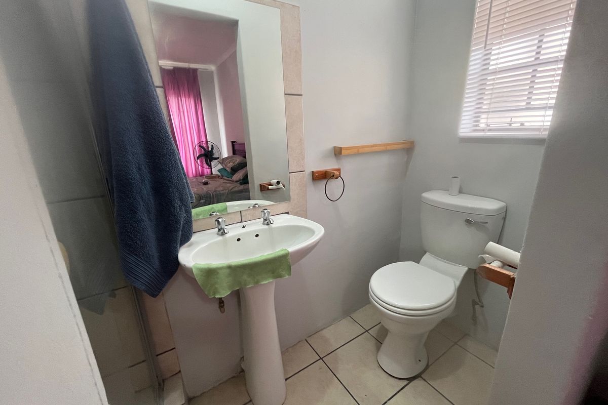 A functional bathroom featuring a pedestal basin, toilet, shower enclosure, and tiled flooring, complemented by natural light from a window with venetian blinds.