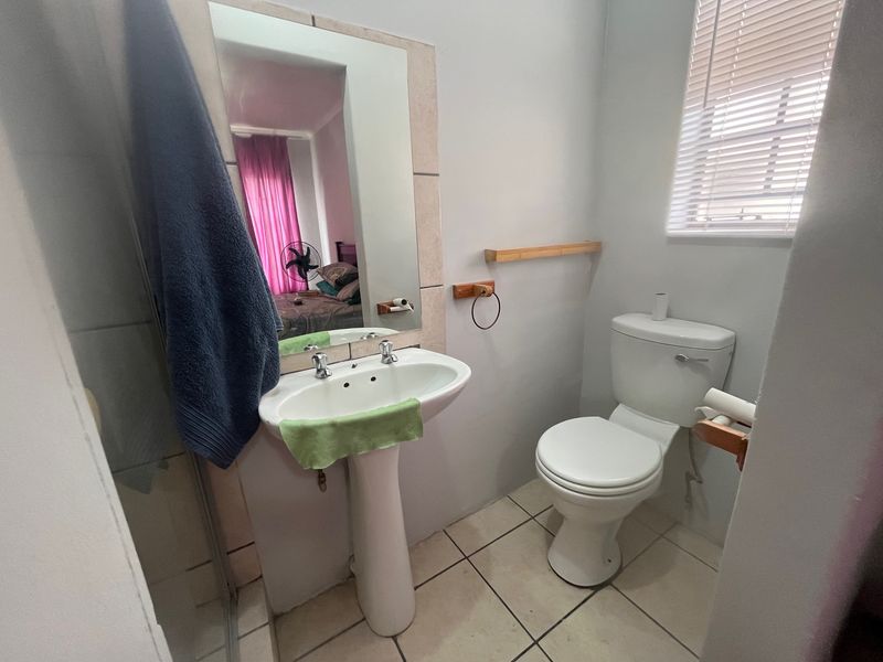 A functional bathroom featuring a pedestal basin, toilet, shower enclosure, and tiled flooring, complemented by natural light from a window with venetian blinds.