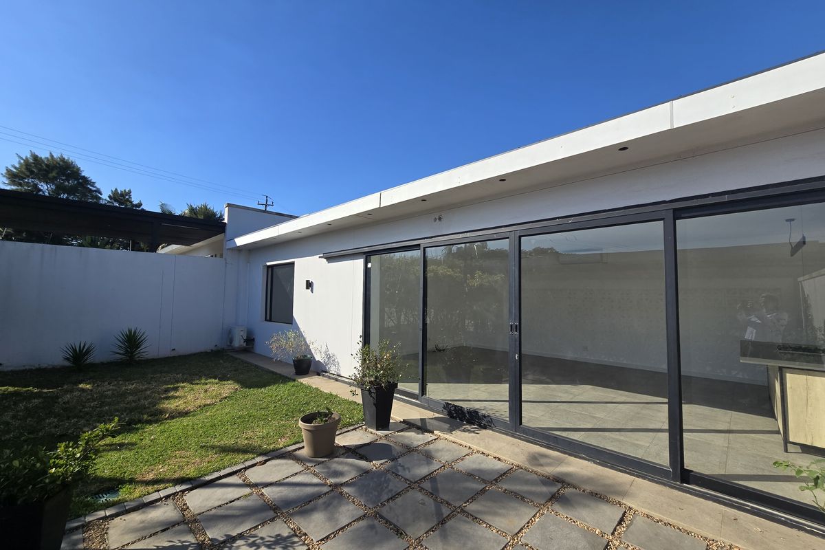 A well-maintained rear exterior featuring a paved patio area, a small lawn, and large sliding glass doors providing seamless indoor-outdoor flow.