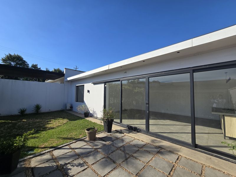 A well-maintained rear exterior featuring a paved patio area, a small lawn, and large sliding glass doors providing seamless indoor-outdoor flow.