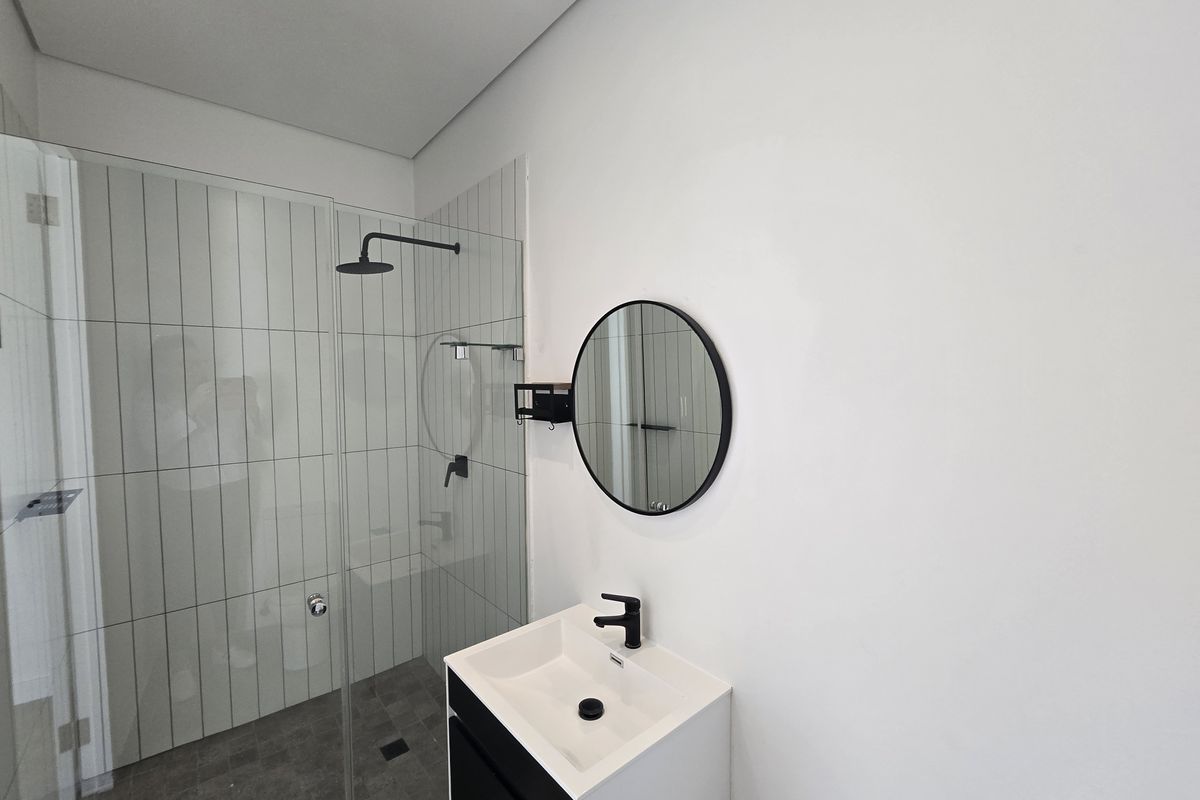 Modern bathroom featuring a walk-in shower with a glass screen, rain shower head, and a contemporary vanity with a black mixer tap.