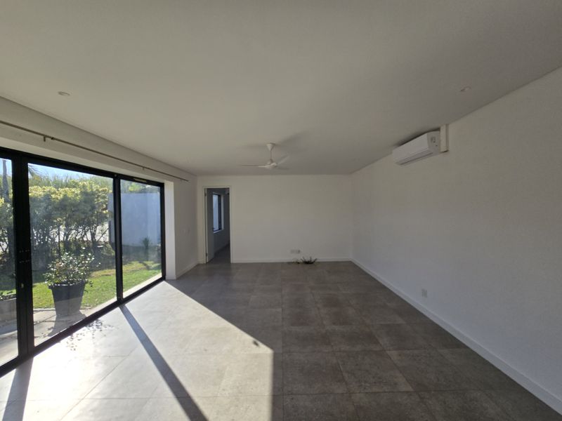 A bright, open-plan living area featuring large sliding glass doors, tiled flooring, a ceiling fan, and a wall-mounted split system air conditioner.