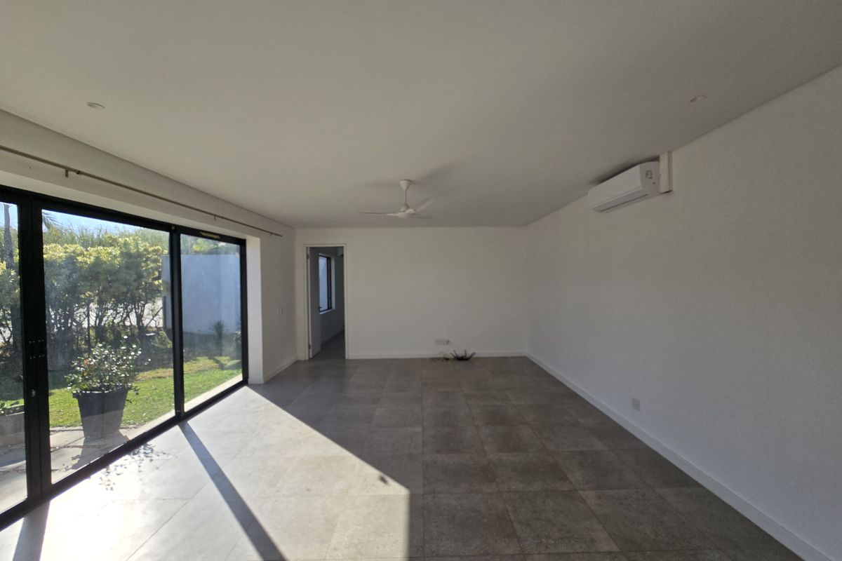 A bright, open-plan living area featuring large sliding glass doors, tiled flooring, a ceiling fan, and a wall-mounted split system air conditioner.