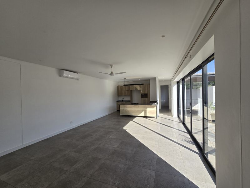 Spacious open-plan living area featuring large format floor tiles, modern kitchen cabinetry with island, and expansive sliding glass doors leading to the patio.