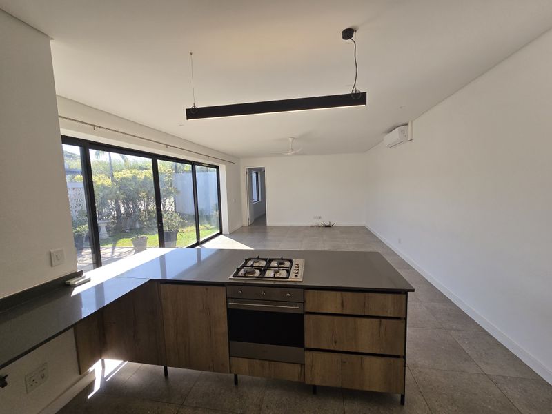 Modern open-plan kitchen and living area featuring a central island with gas hob, sleek cabinetry, tiled floors, and large sliding doors leading to the garden.