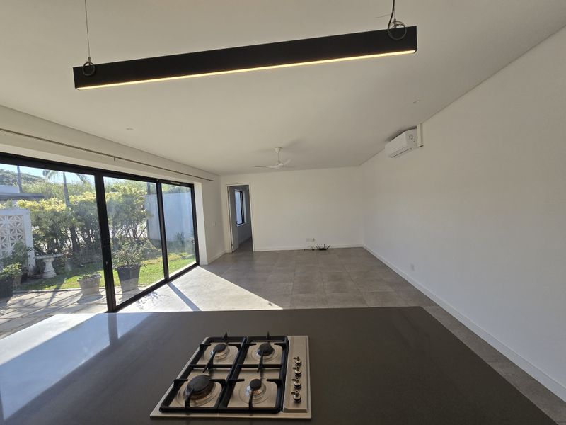 Spacious open-plan living area featuring a modern kitchen island with gas cooktop, tiled floors, and large sliding doors opening to the garden.