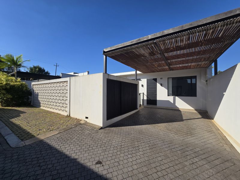 Front exterior view of the townhouse featuring a paved driveway, a timber pergola, and a decorative breeze block wall providing privacy to the entrance.