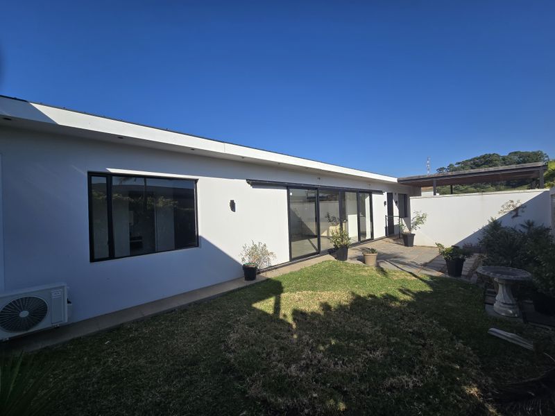 Rear view of the townhouse featuring a paved patio, sliding glass doors, and a private garden area with boundary wall.