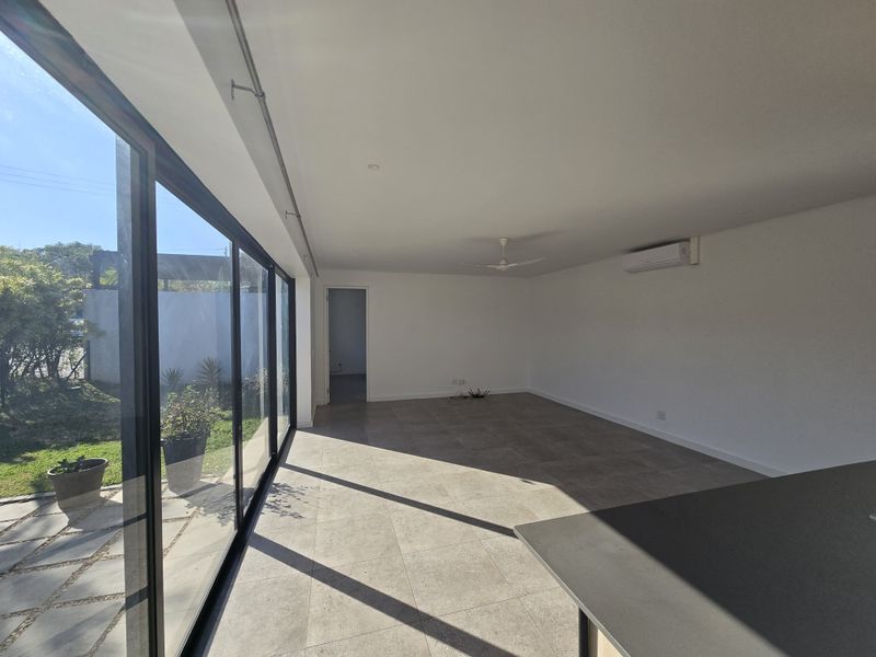 Spacious open-plan living area featuring large sliding glass doors, tiled flooring, a ceiling fan, and a wall-mounted air conditioning unit.