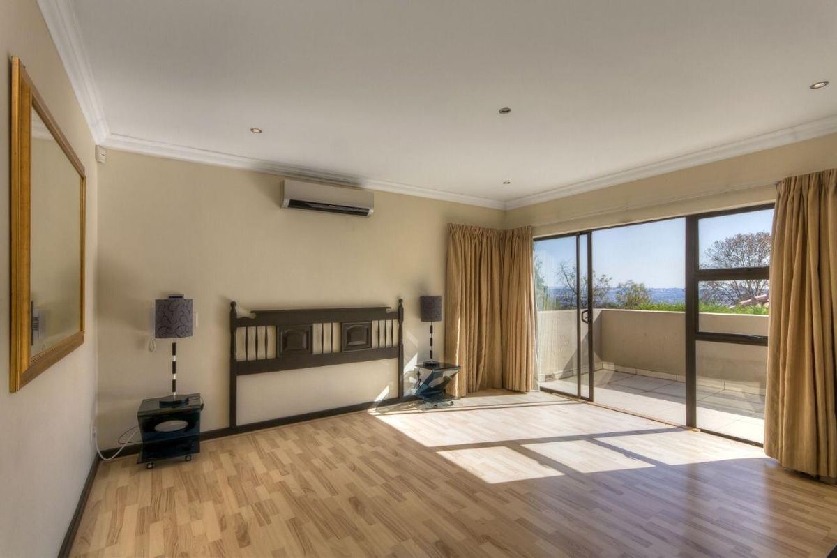 Spacious bedroom featuring light wood-look flooring, a wall-mounted air conditioning unit, and large sliding glass doors opening onto a private balcony with scenic views.