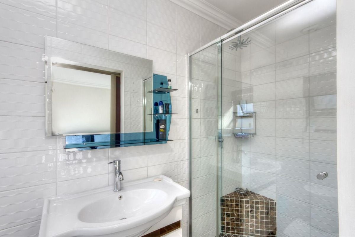 Modern bathroom featuring a white pedestal basin, a glass-enclosed shower with a mosaic-tiled corner seat, and wall-mounted mirror.