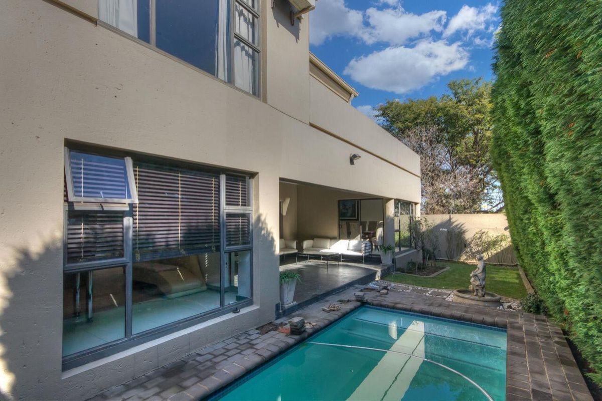 Rear view of the property featuring a covered patio, a swimming pool with paved surround, and a landscaped garden area.