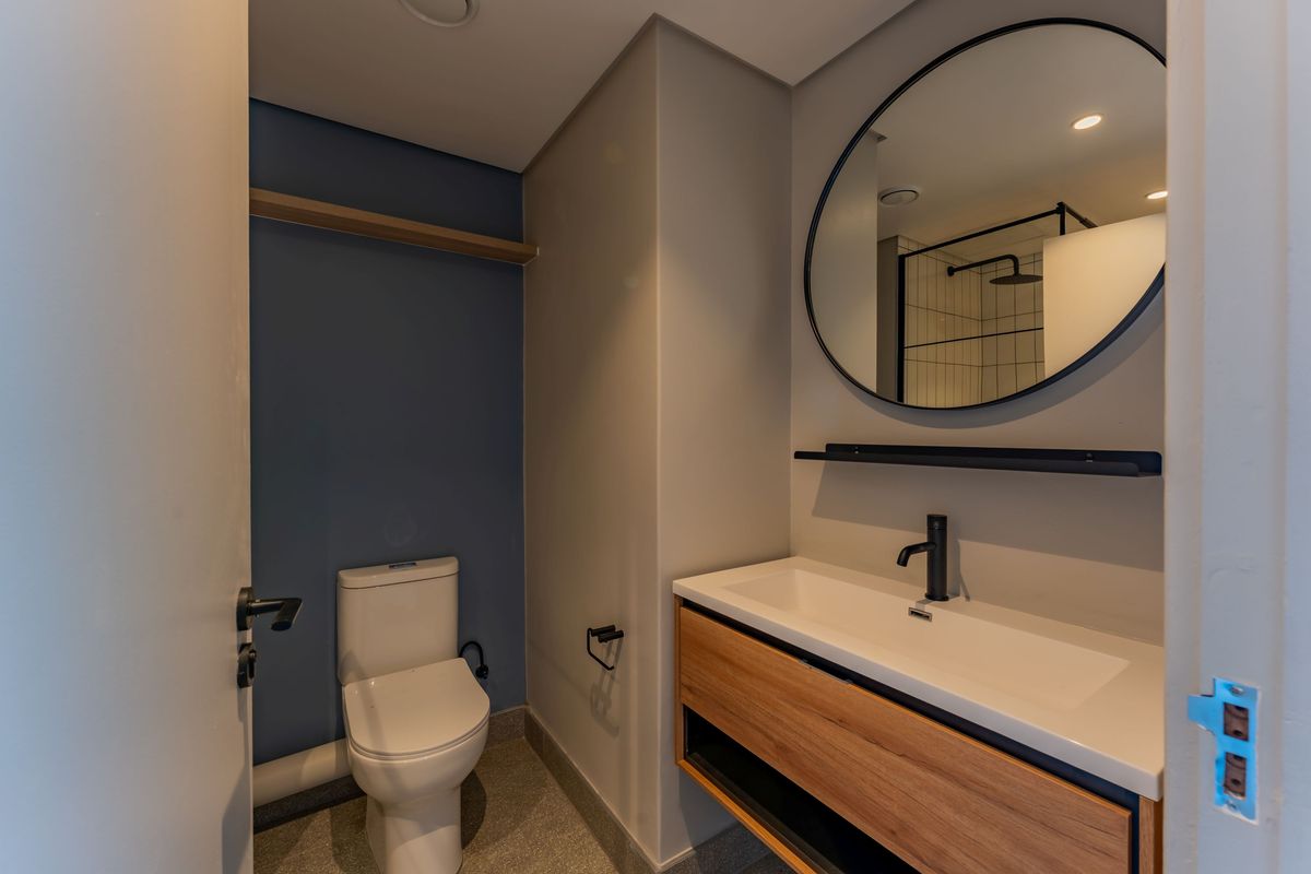 Modern bathroom featuring a floating wood-finish vanity, matte black fixtures, a circular mirror, and a back-to-wall toilet against a blue accent wall.