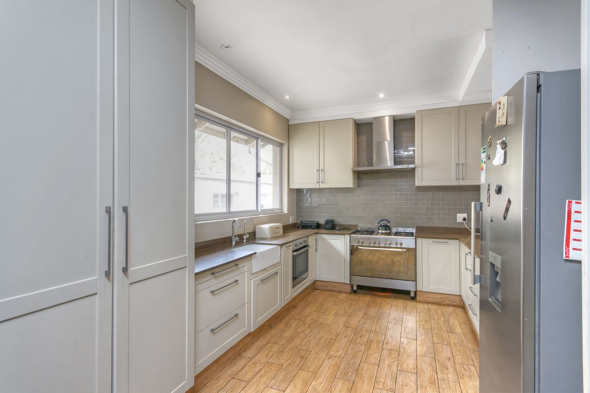 Modern kitchen featuring light-toned cabinetry, subway tile backsplash, stainless steel oven with extractor fan, farmhouse-style sink, and wood-look tiled flooring.