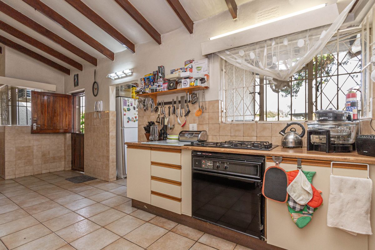 Functional kitchen featuring exposed timber ceiling beams, tiled flooring, built-in oven with gas hob, and ample counter space with wall-mounted storage.