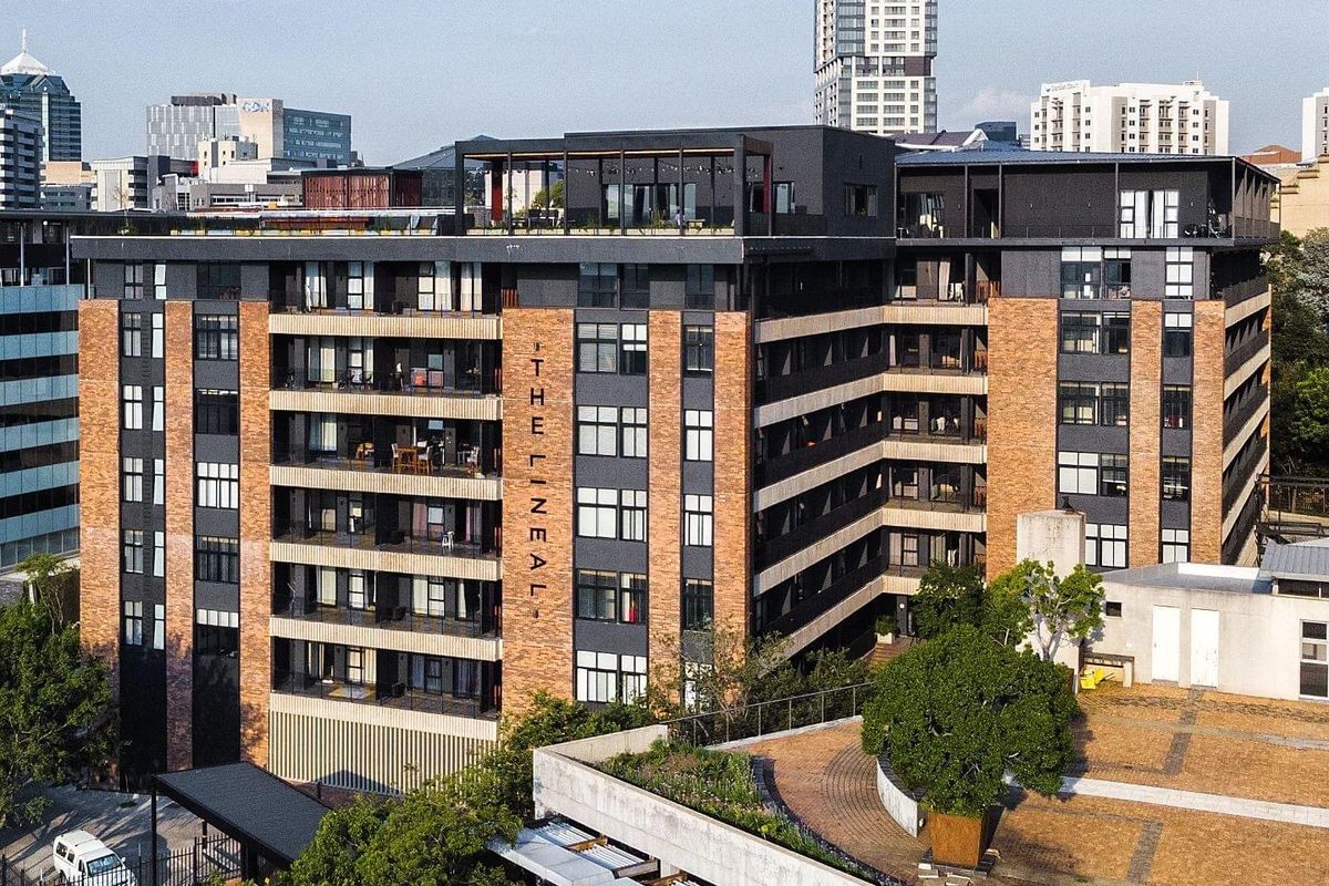 Aerial view of The Lineal apartment complex, showcasing its modern brick and dark facade, balcony levels, and rooftop terrace area.