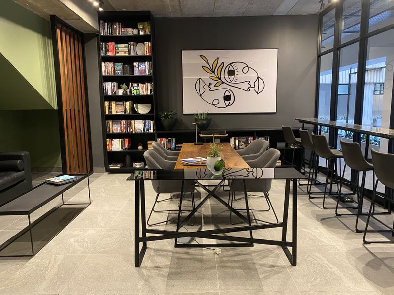 Modern open-plan communal area featuring a built-in floor-to-ceiling bookshelf, exposed concrete ceiling, and large glass partitions.