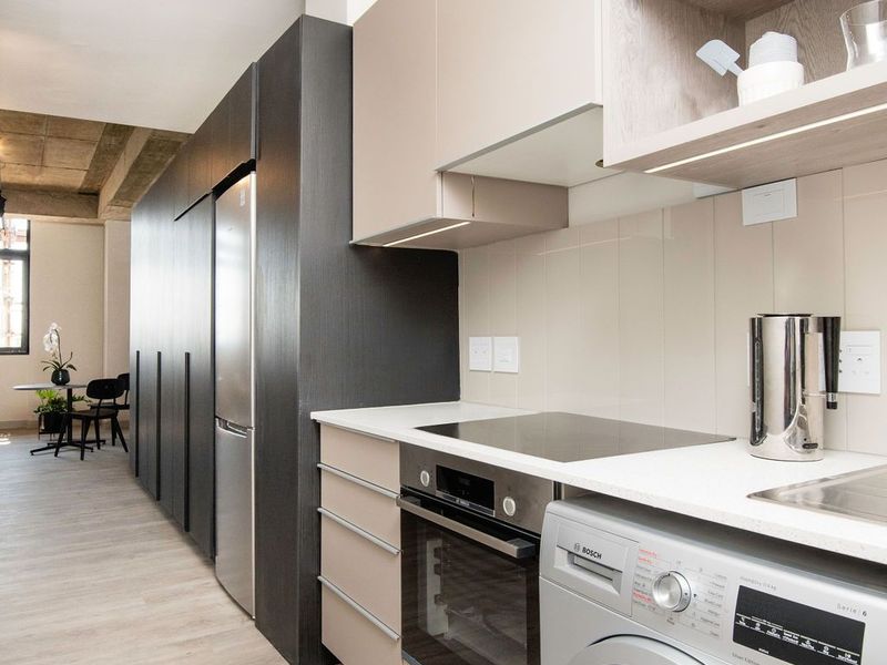 Modern kitchen featuring sleek cabinetry, integrated oven, induction hob, and built-in laundry appliance, seamlessly flowing into the open-plan living area.