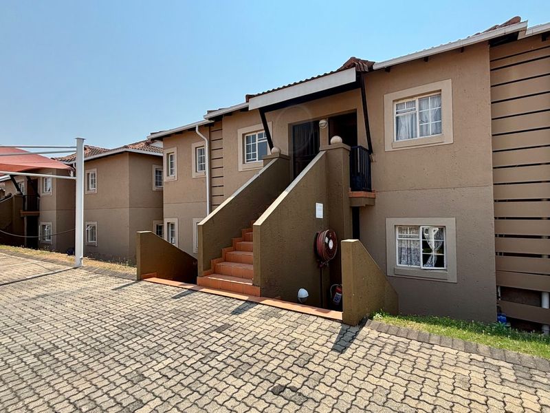 Exterior view of an apartment complex featuring a paved driveway, covered parking, and a staircase leading to the entrance.