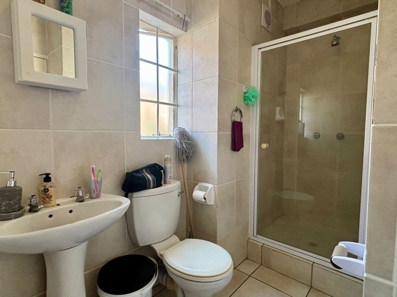 A functional bathroom featuring a pedestal basin, toilet, and a glass-enclosed shower with neutral wall and floor tiling.