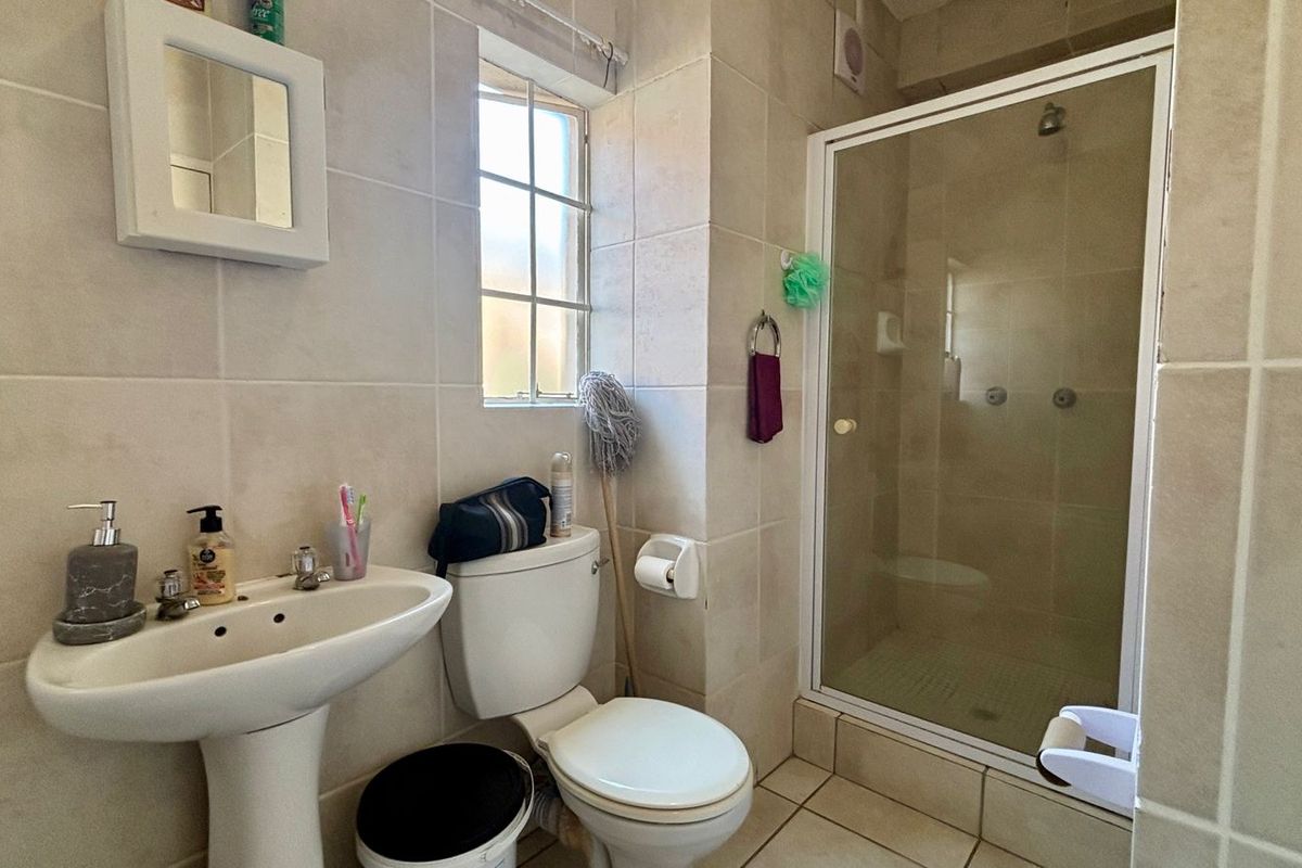 A functional bathroom featuring a pedestal basin, toilet, and a glass-enclosed shower with neutral wall and floor tiling.